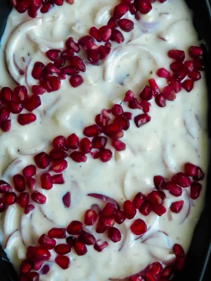 Onion raita in a bowl with thin-sliced onion and yogurt. the raita is also garnished with pomegrantes.