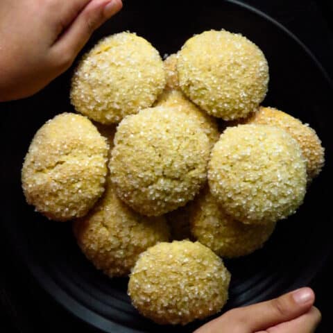 hands holding a plate of gnanakathai(sugar coated cookies)