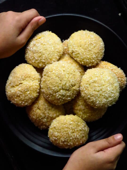hands holding a plate of gnanakathai(sugar coated cookies)