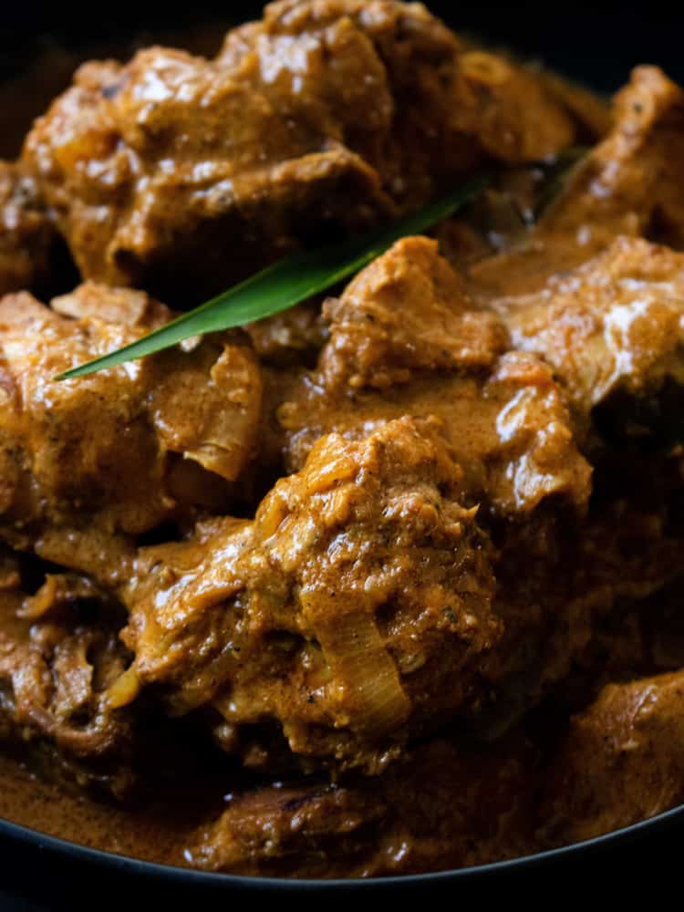 Sri Lankan chicken curry with pandan leaf as garnish, placed in a black bowl.