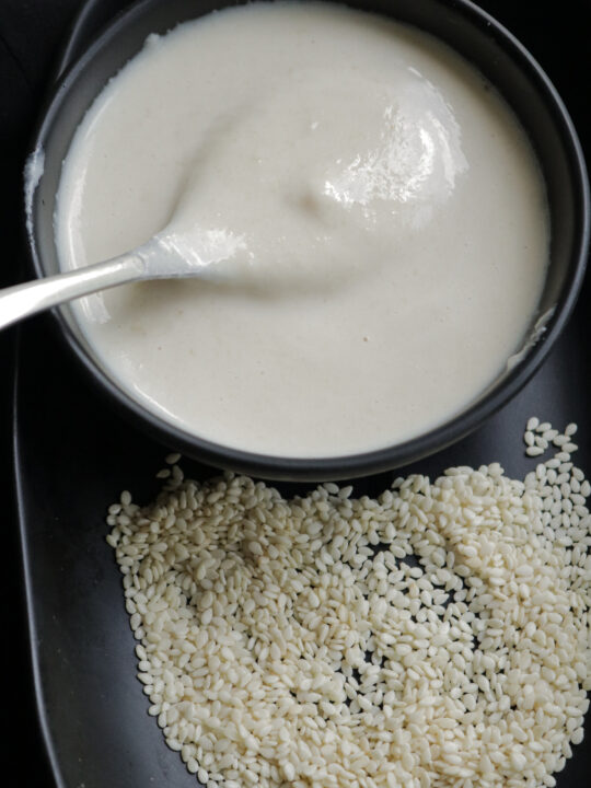 homemade tahini in a bowl with a spoon of tahini and sesame seeds