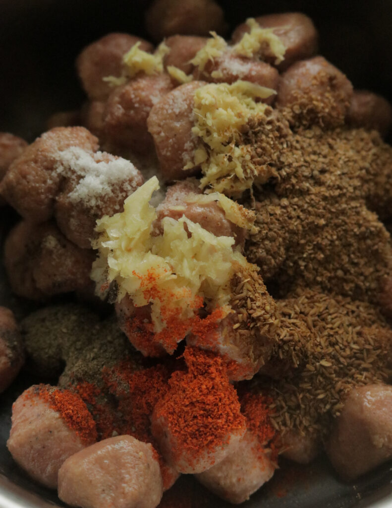 adding spices and minced ginger garlic to marinate the meatballs.