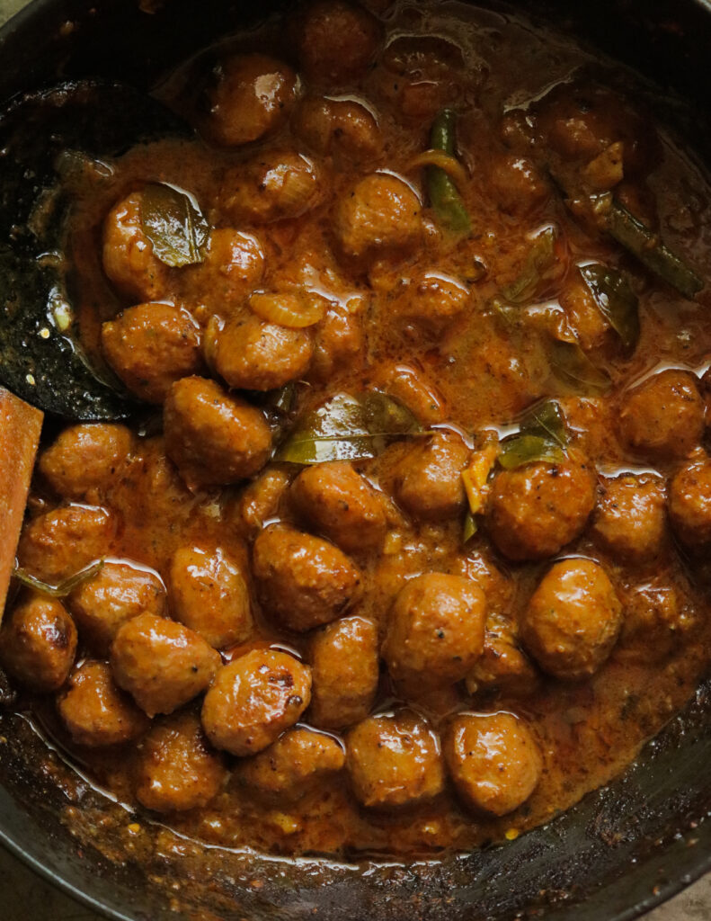 thick meatball curry scooped with a wooden spoon.