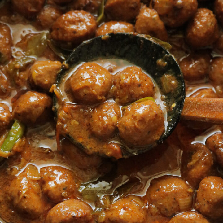 a pan of chicken meat ball curry with a wooden spoon full of meatballs