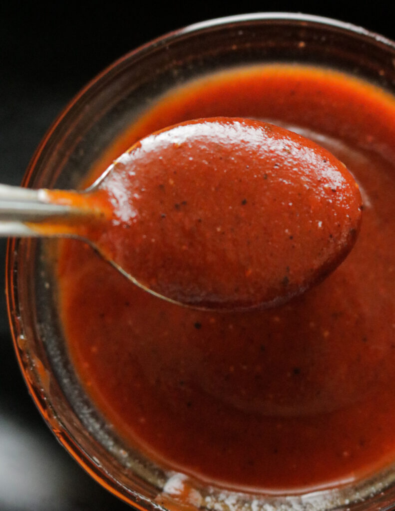 Sweet and spicy BBQ sauce in a container and scooped with a spoon.