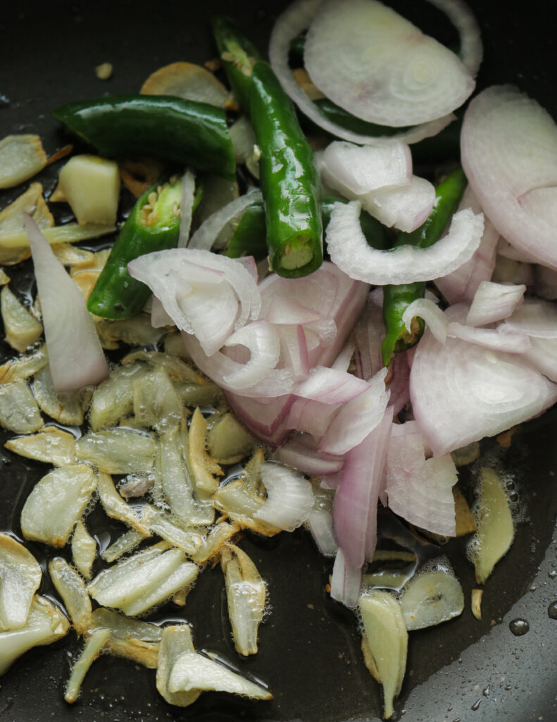 Adding sliced onions to the frying garlic slice to make chilli chicken recipe.