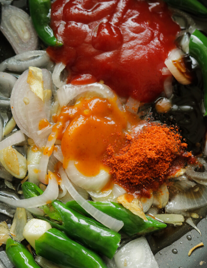 adding tomato sauce, hot sauce , chilli powder and green chillies to make the chilli chicken.