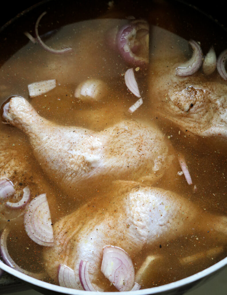 chicken quarters with skin covered in water, spices onions to make chicken broth for mandi rice.
