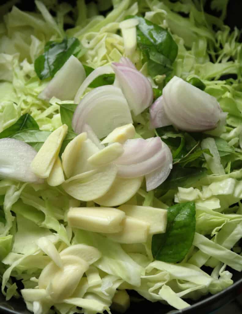 raw cabbage sliced, sliced garlic, sliced onions and curry leaves.