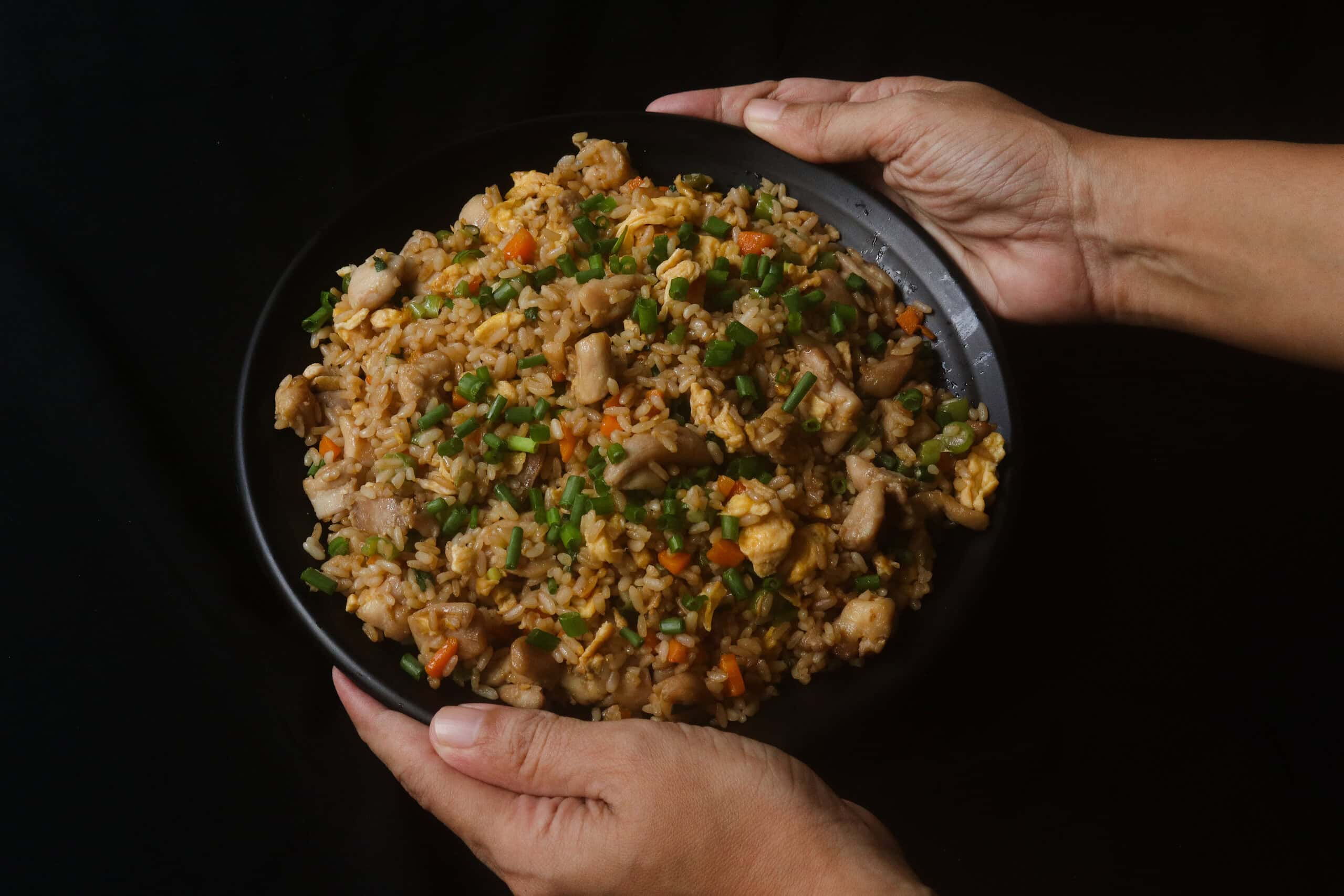 chicken fried rice served in a black platter with pieces of chicken and eggs.