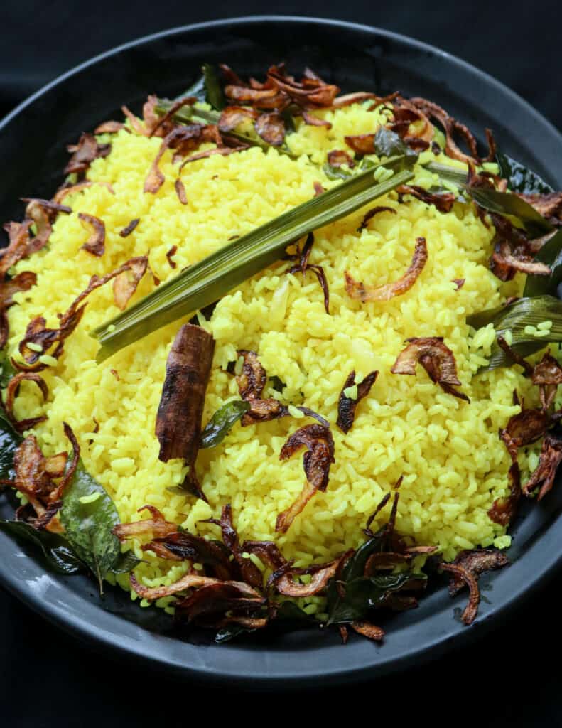 fragrant Sri Lankan yellow rice with fried garnish arounf the rice and served in a black platter.