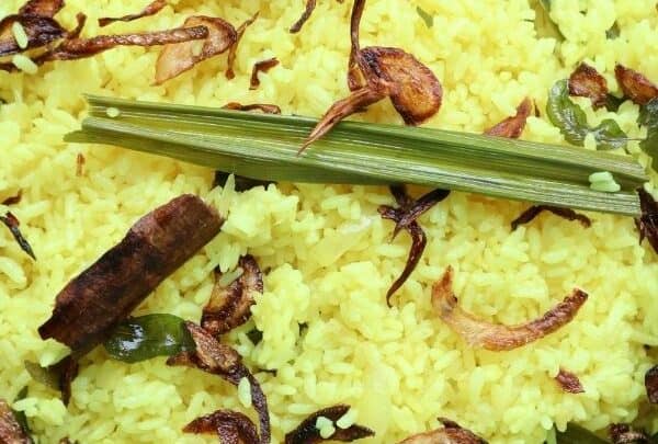 Sri Lankan yellow rice served on a black platter, garnished with fried onions and pandan leaf.
