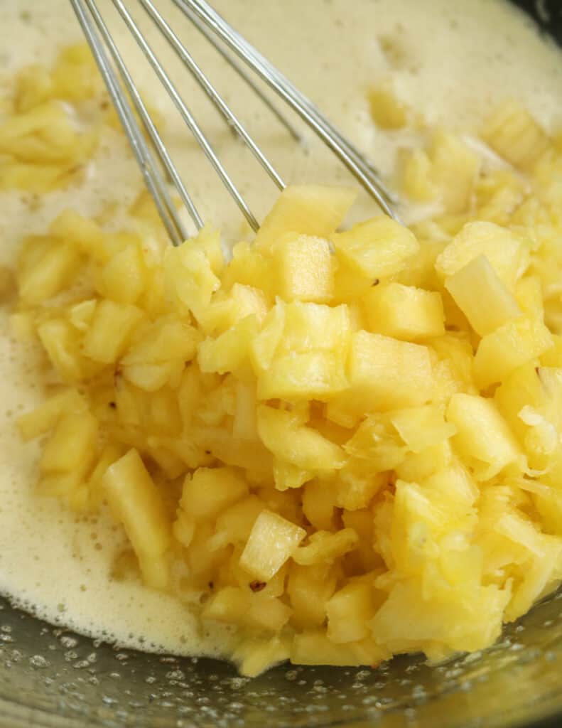 adding the chopped pineapple pieces to the whisked egg and sugar to make the pineapple bread pudding.