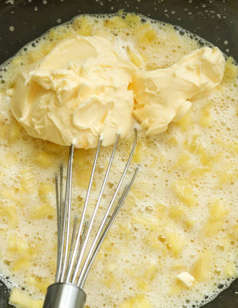 adding butter to the whisked eggs and pineapple to make the pineapple bread pudding.