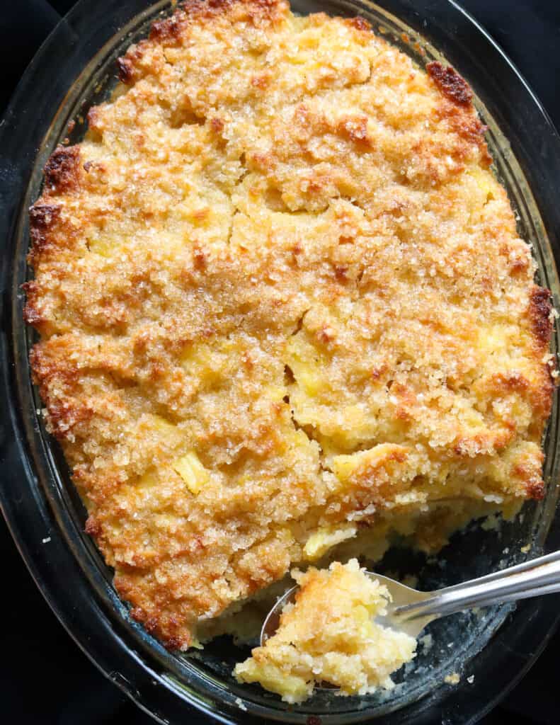 baked pineapple bread pudding with a spoon scooping a piece of it with a spoon.