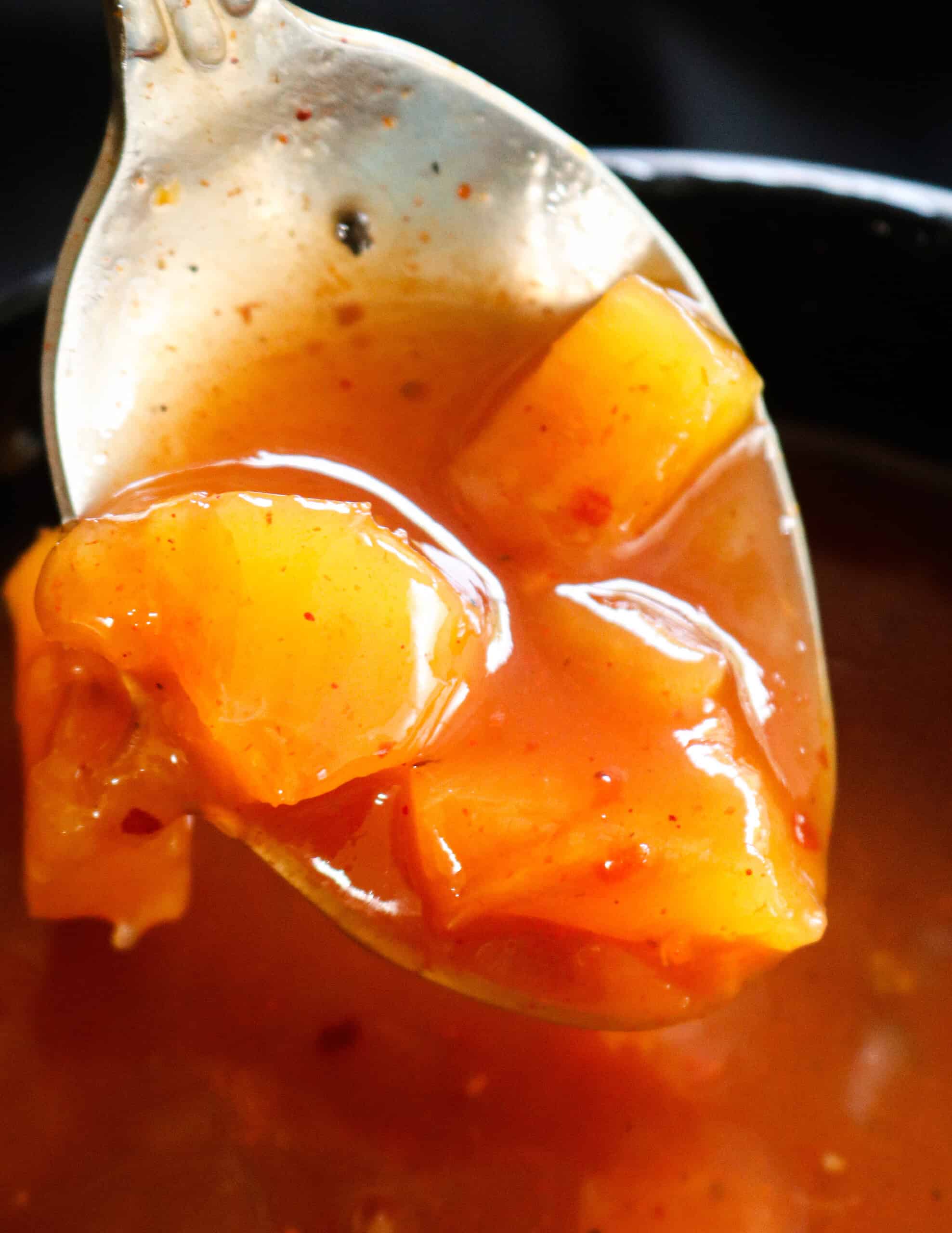 sweet and sour recipe with pineapple chunks scooped in a spoon.