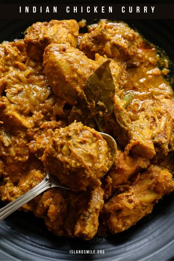 Indian chicken curry served in a plate with a spoon scooping a piece of chicken.