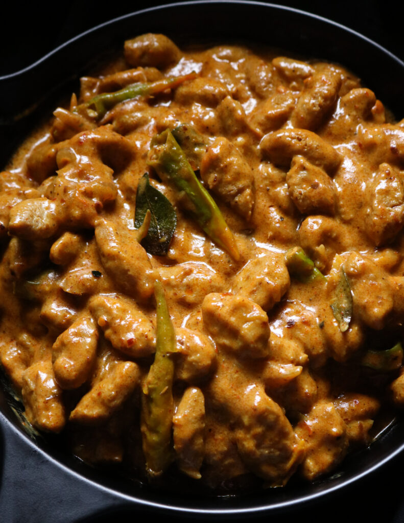 thick soya meat curry cooked in coconut milk with curry leaves and green chillies. served in a black bowl.