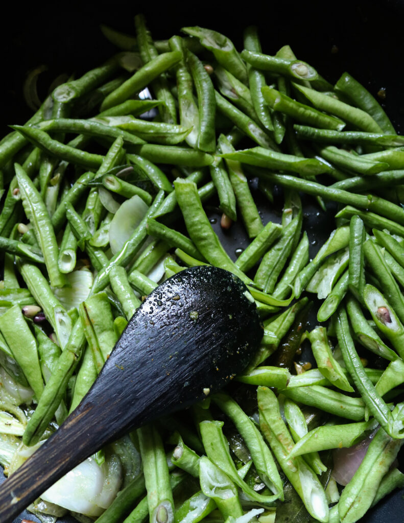 adding long beans to the cooking onions and sliced garlic.