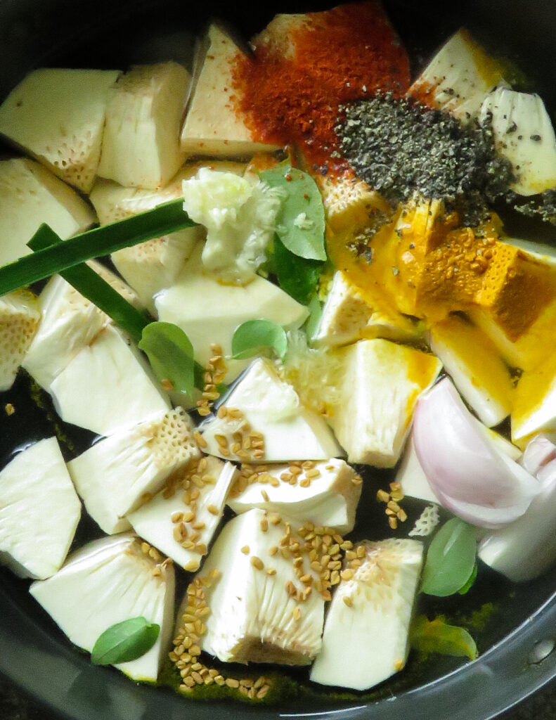 adding onions, fenugreek seed, curry leaves into a cooking pot to make the bread fruit curry