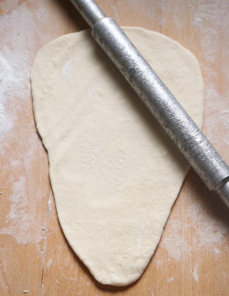 stretching the dough on a flour board with a rolling pin.
