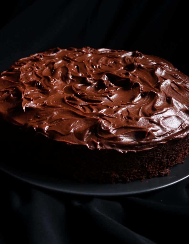 single layer chocolate cake with frosting on top placed on a black plate.
