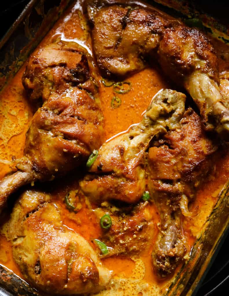 baked curry chicken quarters with a curry sauce in a Pyrex dish.