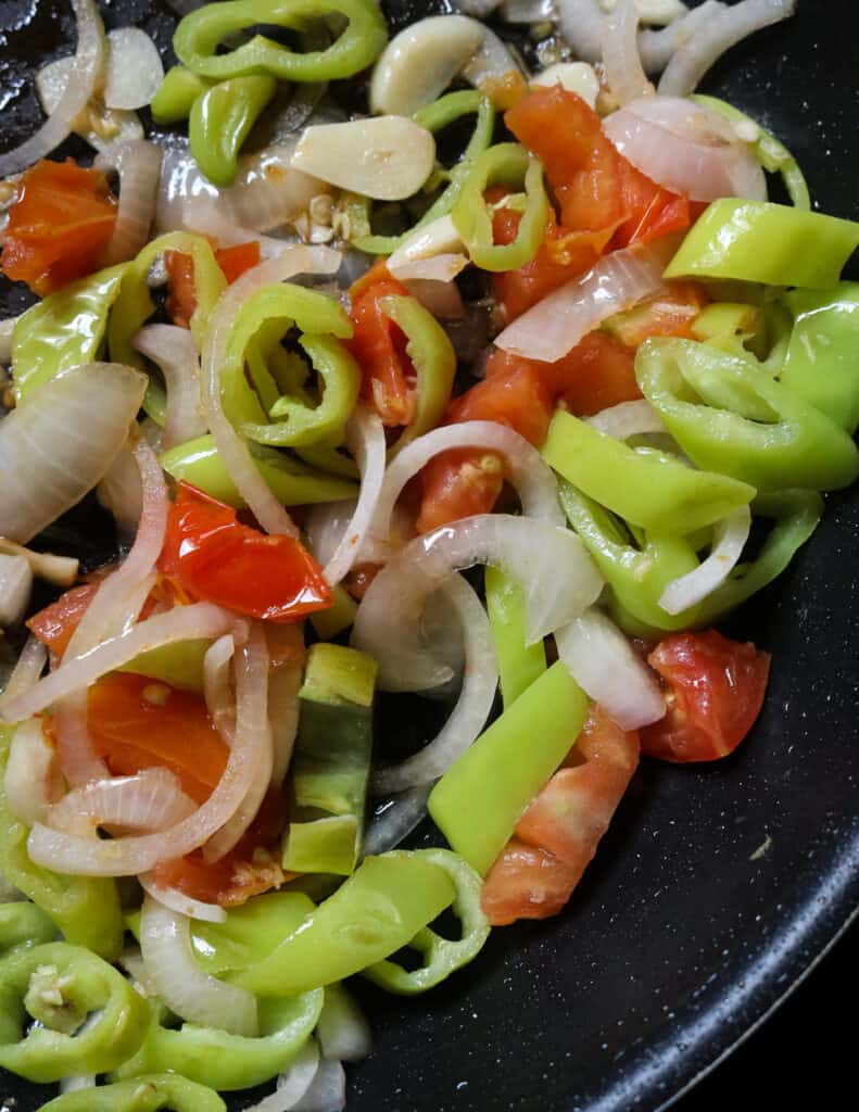 sliced onions, green peppers and tomatoes cooked in a frying pan in oil