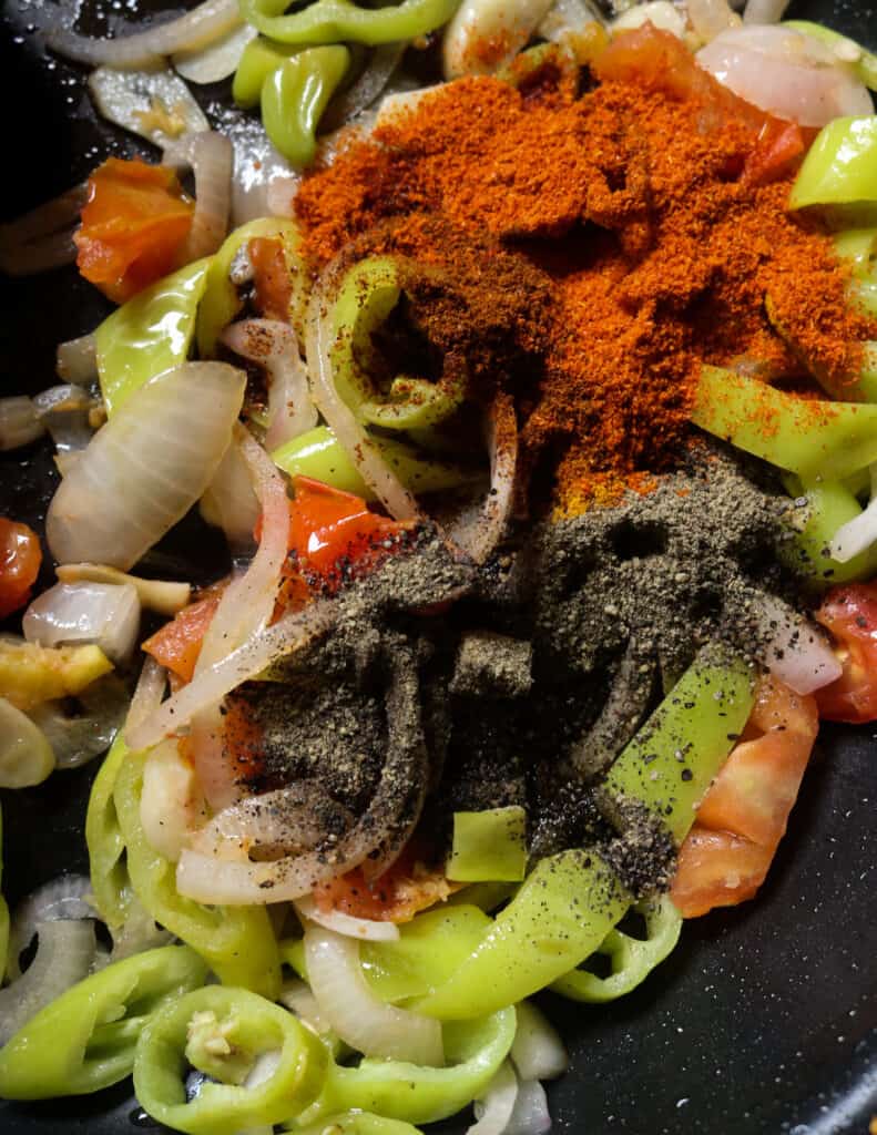 adding black peppers, red chilli powder to the cooking onions, tomatoes and green peppers