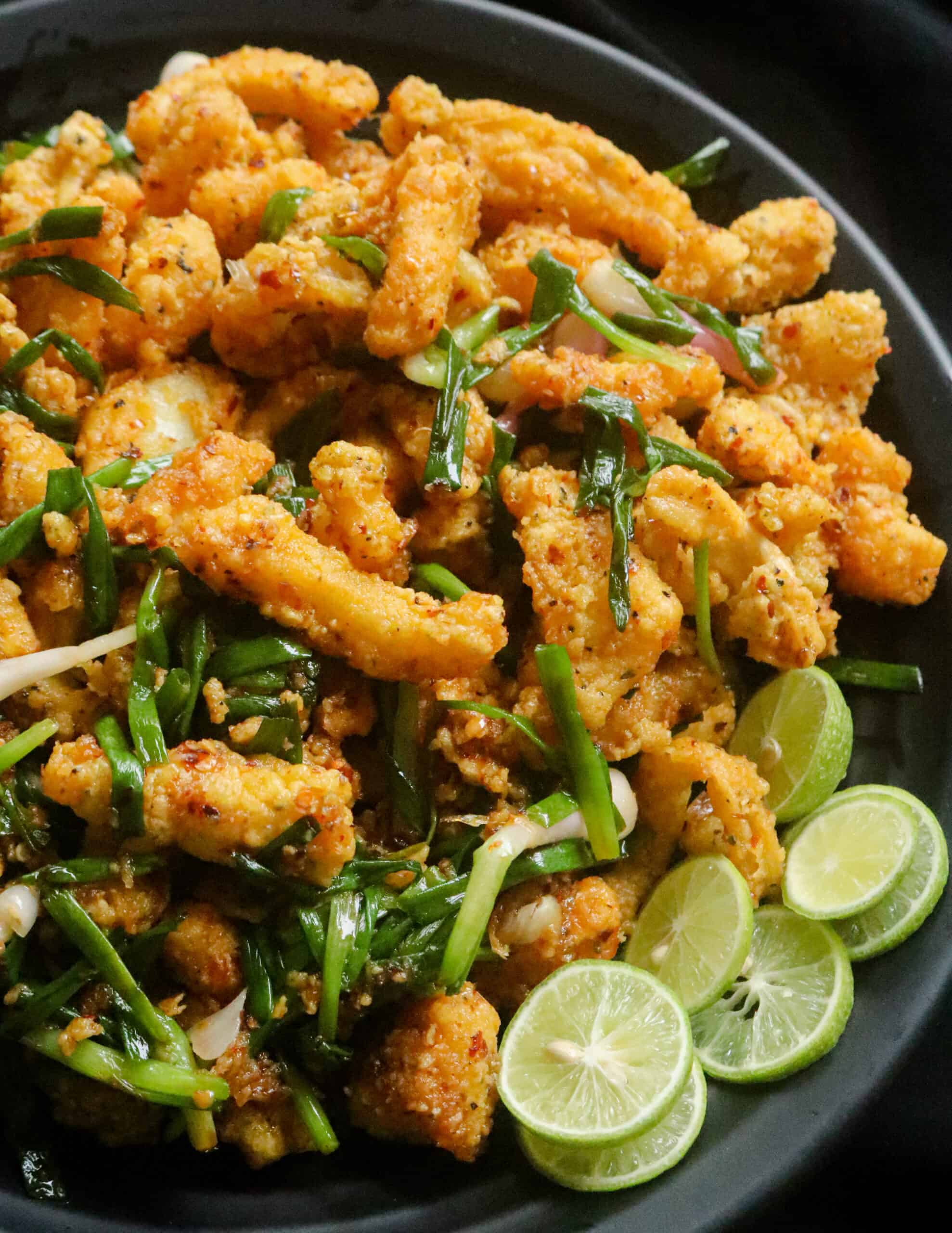 fried cuttlefish with scalions and served in a black plate with lime wedges.