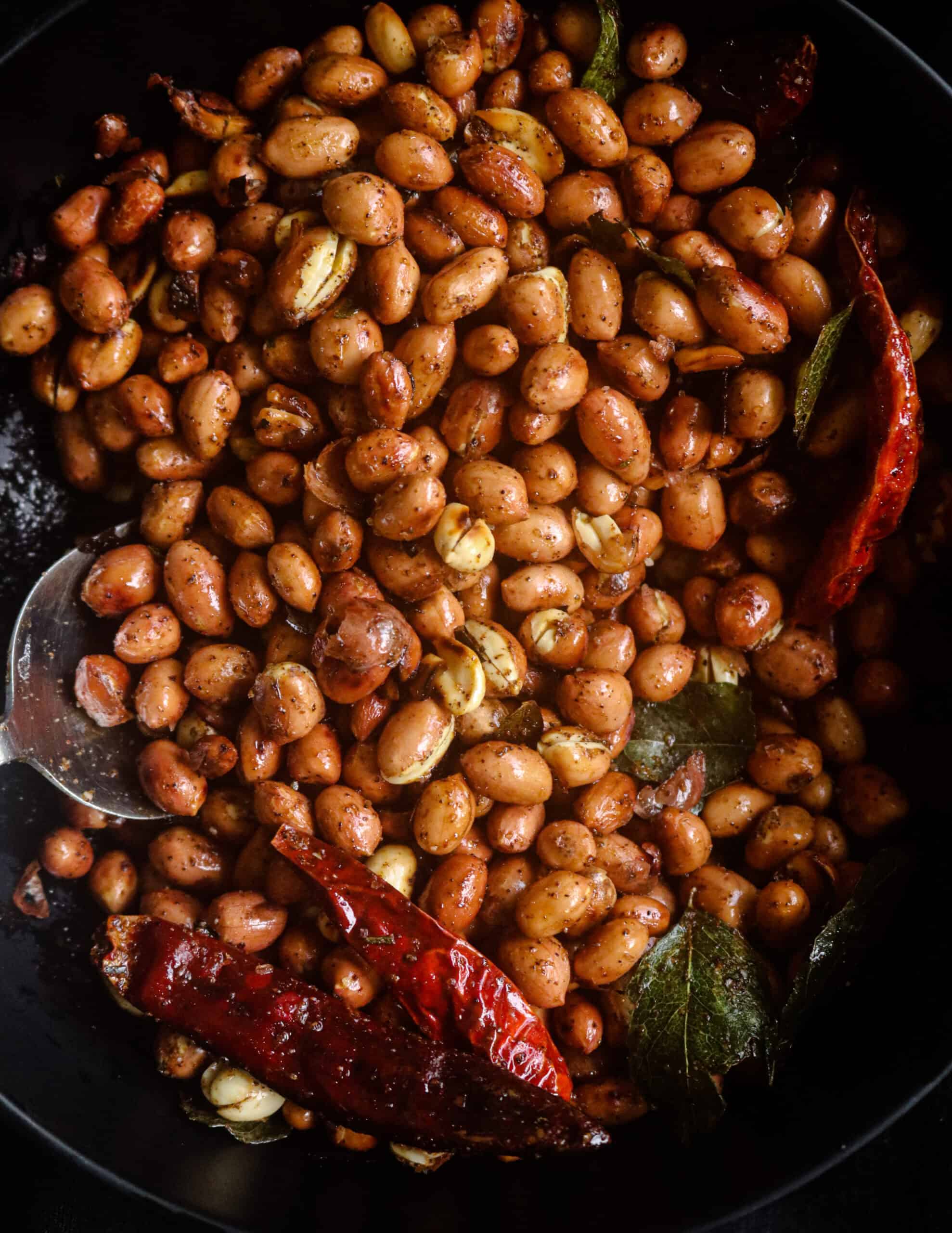 roasted crunchy peanuts served on a bowl with dried red chillies and curry leaves.