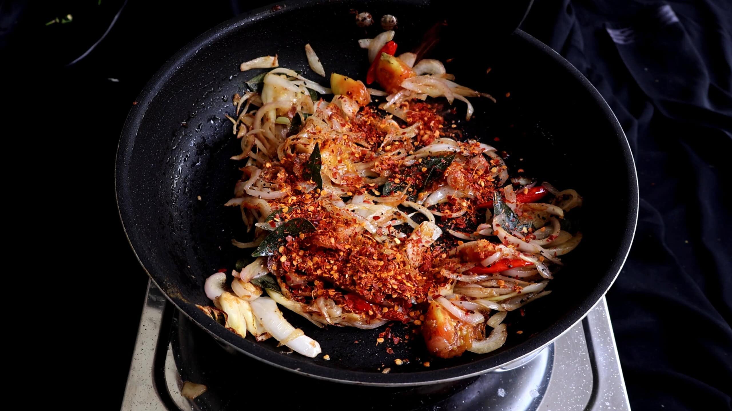 adding red chilli flakes to cook spicy prawn stir fry.
